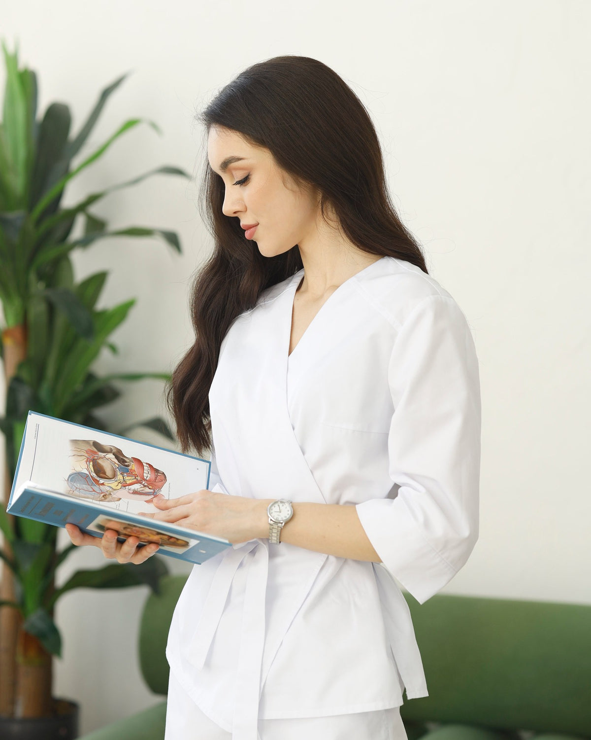 Daria, licensed esthetician and certified acne expert at KUDARI, holding a facial anatomy atlas in her treatment room
